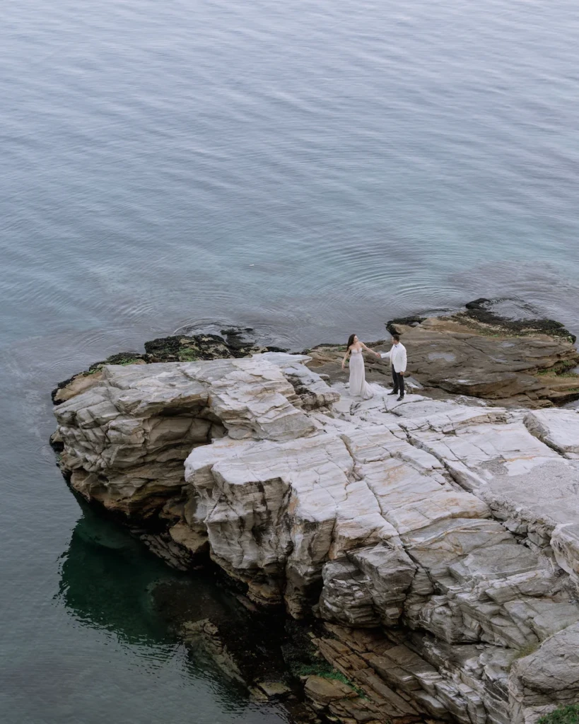 Anastasia and Aggelos walking together along the coast in their wedding attire