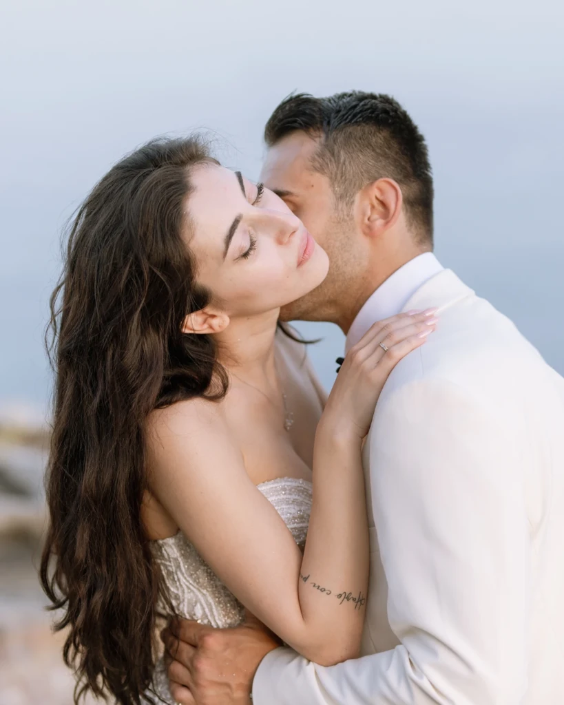 Anastasia and Aggelos in a tender embrace by the sea at golden hour after their wedding