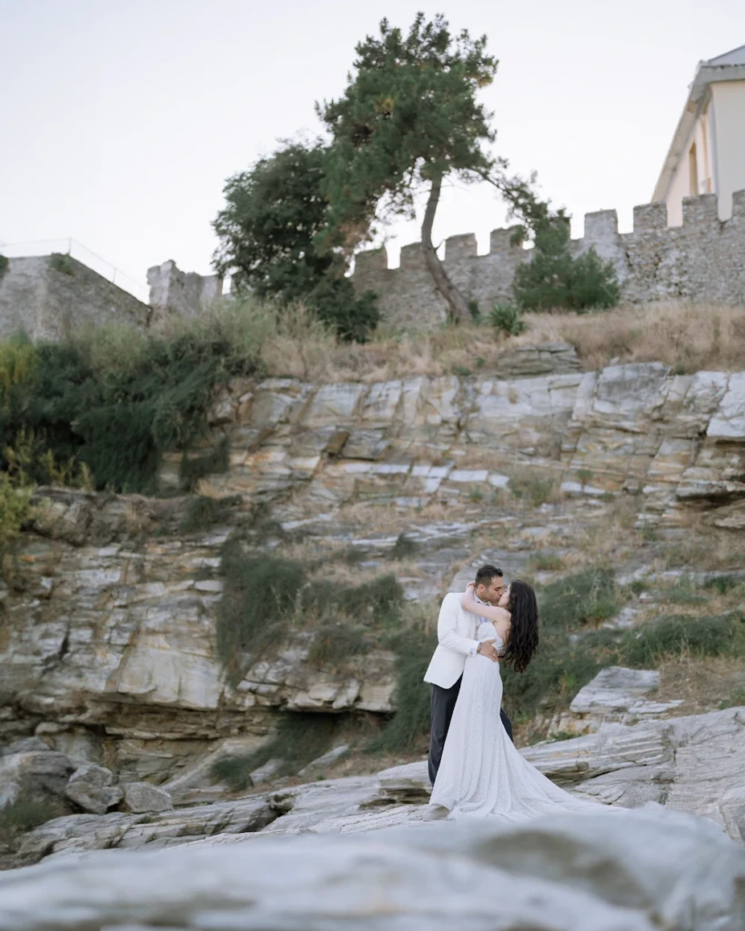 Anastasia and Aggelos embracing on the white marble shoreline by the sea