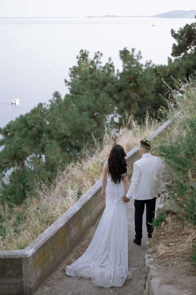 Anastasia and Aggelos walking a coastal path in Kavala old town, the fortress and sea behind them