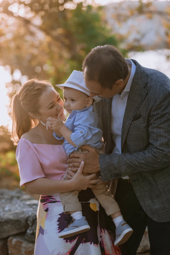 Mother and father in warm golden light leaning close around their baby boy after his baptism
