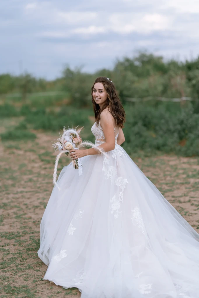 Bride Elena holding her bouquet in a countryside orchard during a rustic wedding photoshoot
