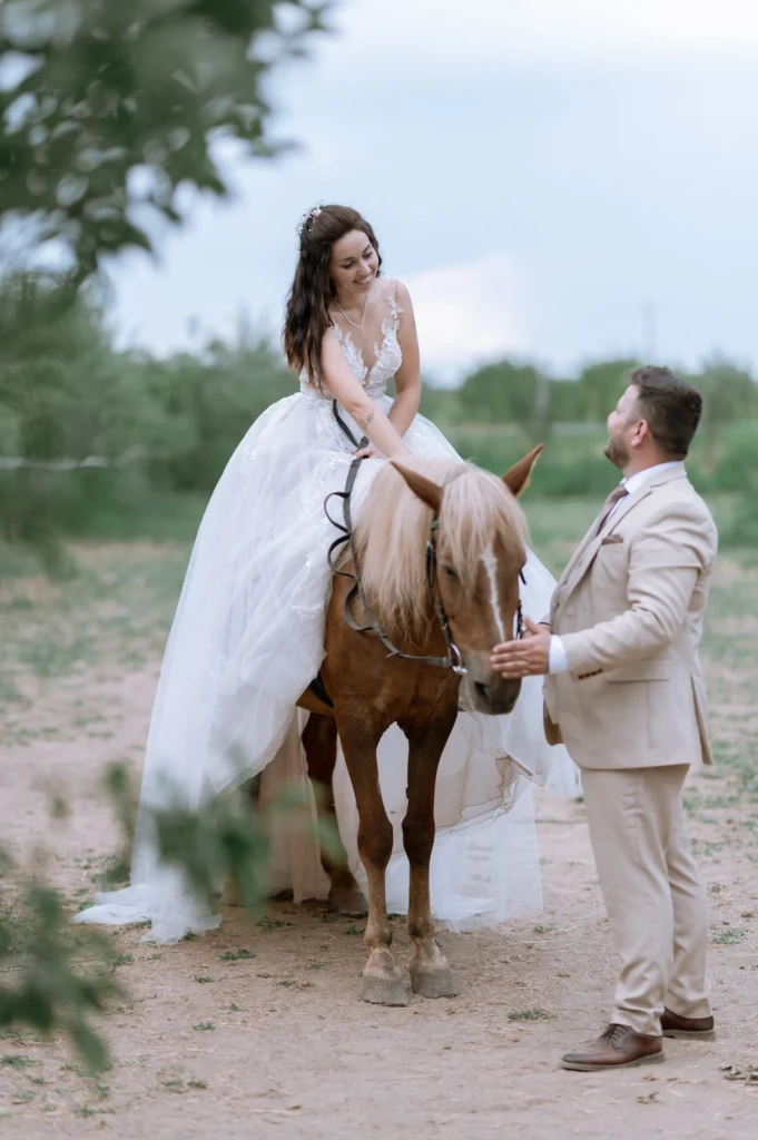 Elena and Vasilis laughing together beside their horse in a green field