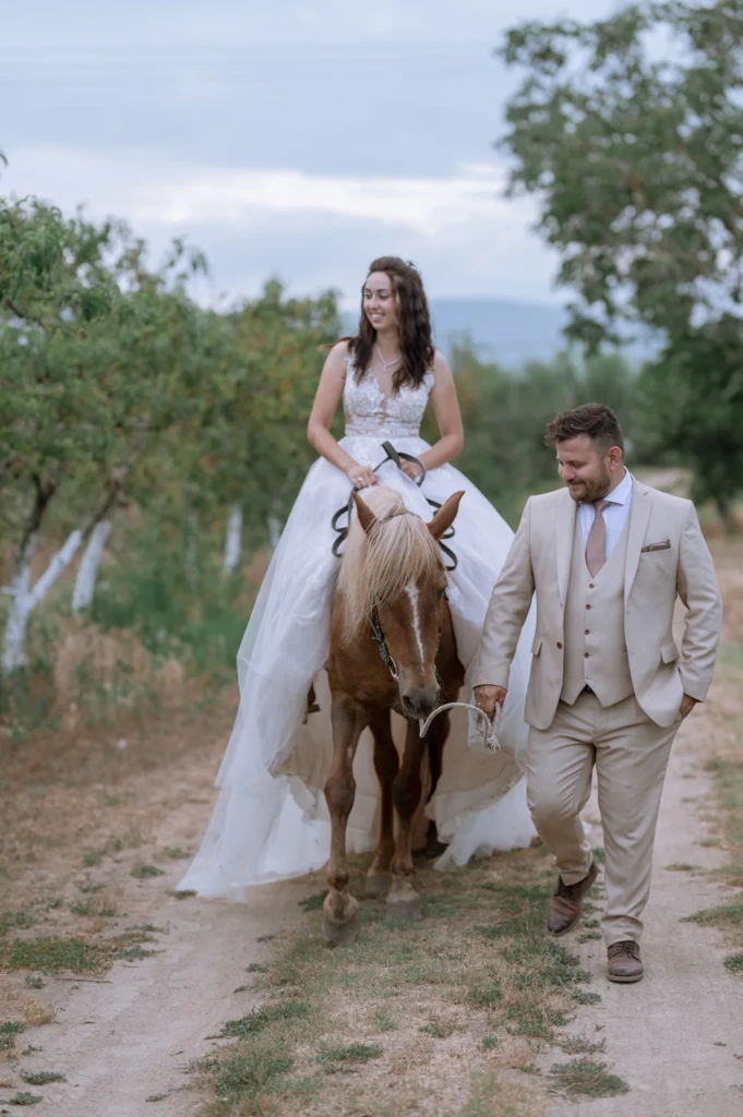 Elena riding a horse which is led by Vasilis along the countryside