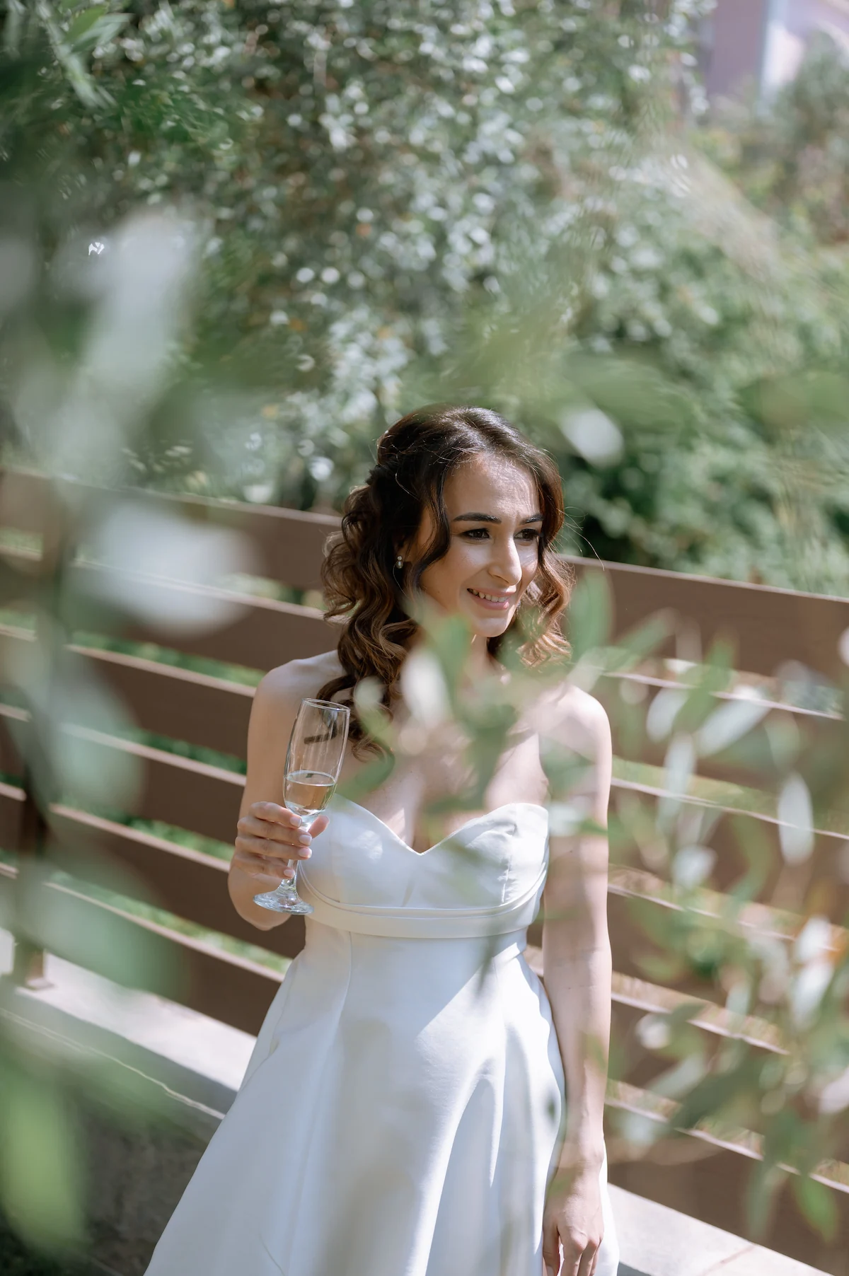 Bride Eva laughing with a glass of champagne in the garden before the wedding