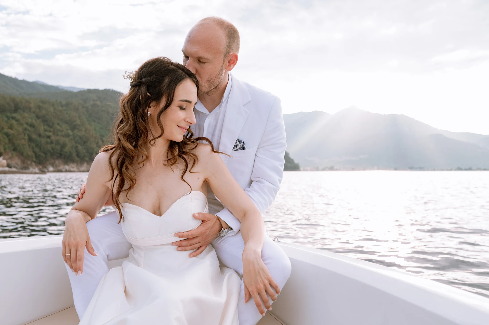 Eva and Stavros embracing on a boat with mountains across the bay in golden light