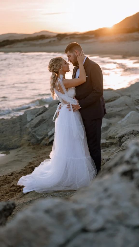 Fenia and Dimitris embracing on the rocks by the sea at golden hour
