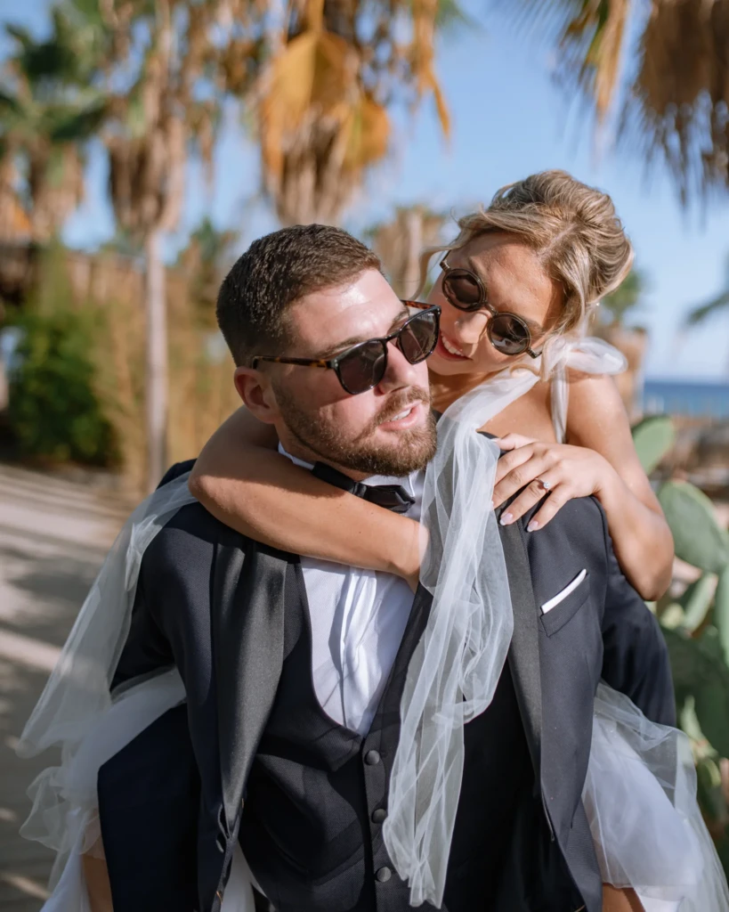 Fenia and Dimitris walking hand in hand beneath palm trees on their wedding day