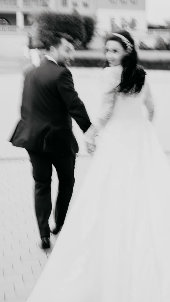 Loukiani and Giorgos looking back as they walk hand in hand at Ktima Biblia Chora, motion-blur black and white