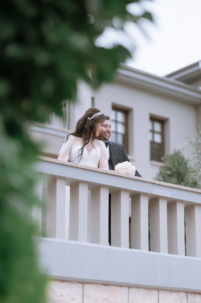 Loukiani and Giorgos laughing together on a balcony at Ktima Biblia Chora, framed by greenery