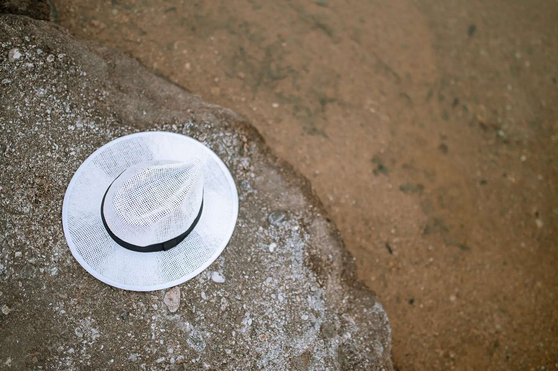 White wide-brim summer hat resting on a sunlit rock by the sea — MOA wedding & christening photography, Kavala